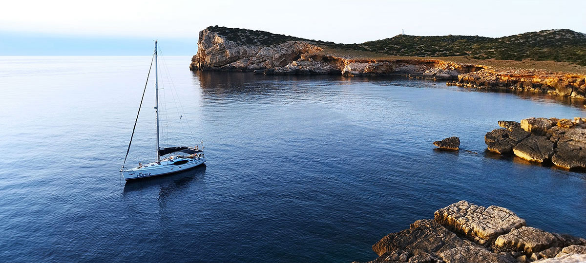 A single yacht at anchor in a blue bay on the Ibiza coast