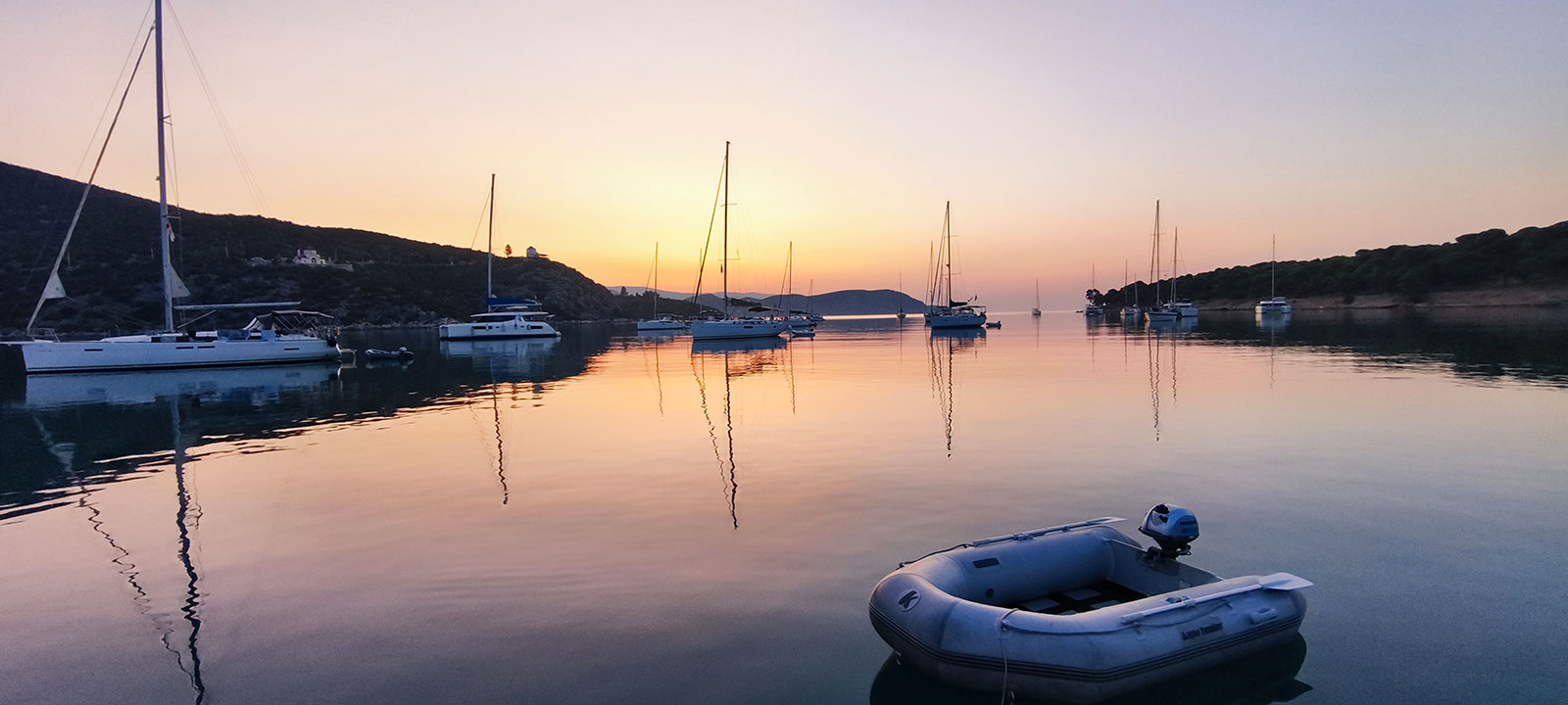 Des voiliers au mouillage sur une mer d'huile, au coucher du soleil