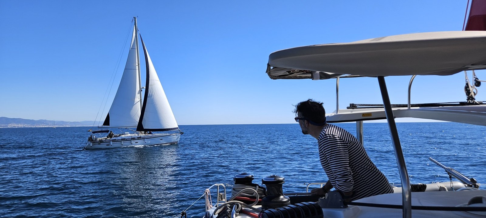 A yacht under sail seen from the deck of a catamaran