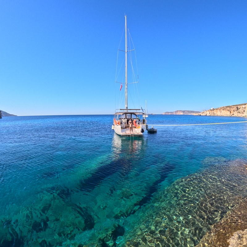 A yacht at anchor over clear turquoise water off Kimolos, Cyclades, Greece