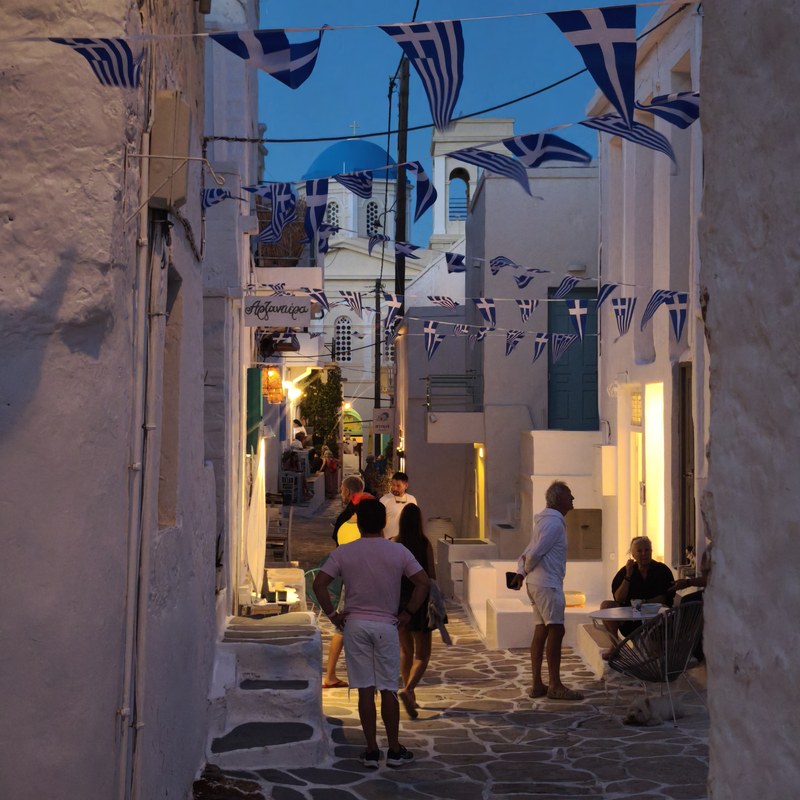 A whitewashed lane strung with Greek flags in the evening, Kimolos, Cyclades