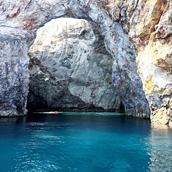 A rock arch over deep blue water in the strait between Kimolos and Polyaigos
